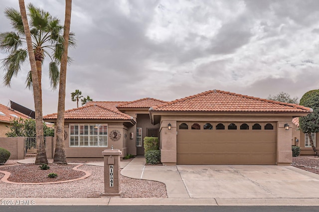 mediterranean / spanish house with fence, a tiled roof, stucco siding, driveway, and an attached garage