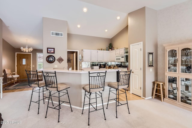 kitchen featuring white microwave, visible vents, a peninsula, a kitchen bar, and a notable chandelier