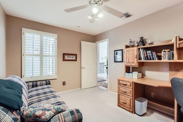 office space featuring baseboards, visible vents, ceiling fan, built in desk, and light colored carpet