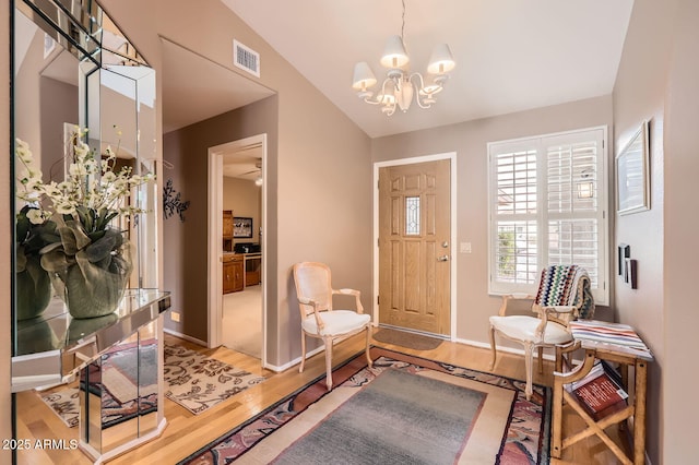 foyer entrance featuring visible vents, baseboards, lofted ceiling, light wood-style flooring, and a notable chandelier