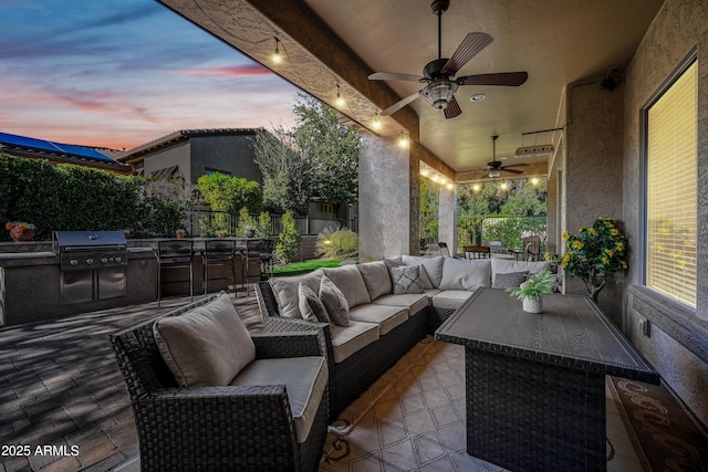 patio terrace at dusk featuring grilling area, an outdoor kitchen, outdoor lounge area, and ceiling fan