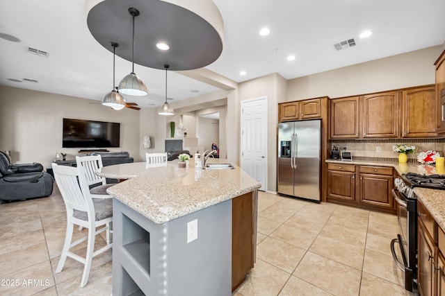 kitchen featuring pendant lighting, sink, appliances with stainless steel finishes, light stone counters, and an island with sink