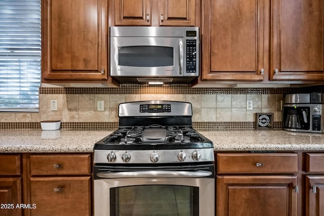 kitchen featuring appliances with stainless steel finishes, light stone countertops, and decorative backsplash