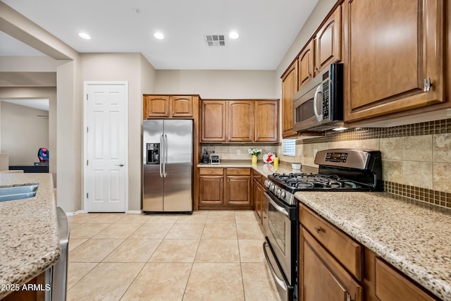 kitchen featuring tasteful backsplash, light tile patterned flooring, appliances with stainless steel finishes, and light stone counters