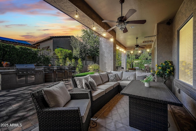 patio terrace at dusk with an outdoor living space, a grill, ceiling fan, and an outdoor kitchen