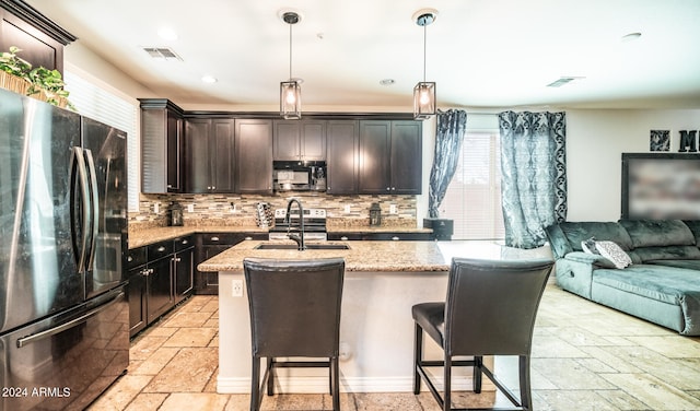 kitchen with backsplash, a kitchen island with sink, refrigerator, sink, and hanging light fixtures