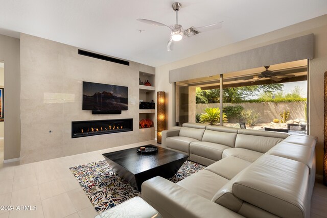 tiled living room featuring built in features, ceiling fan, and a large fireplace