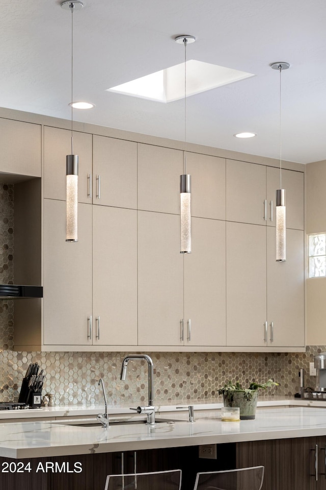 kitchen featuring wall chimney range hood, tasteful backsplash, pendant lighting, and cream cabinetry