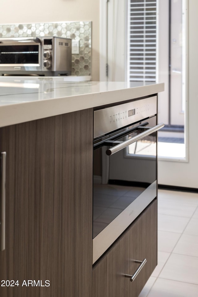 kitchen with light tile patterned flooring, oven, a toaster, backsplash, and modern cabinets