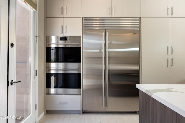 kitchen featuring light tile patterned floors, modern cabinets, appliances with stainless steel finishes, and light stone counters