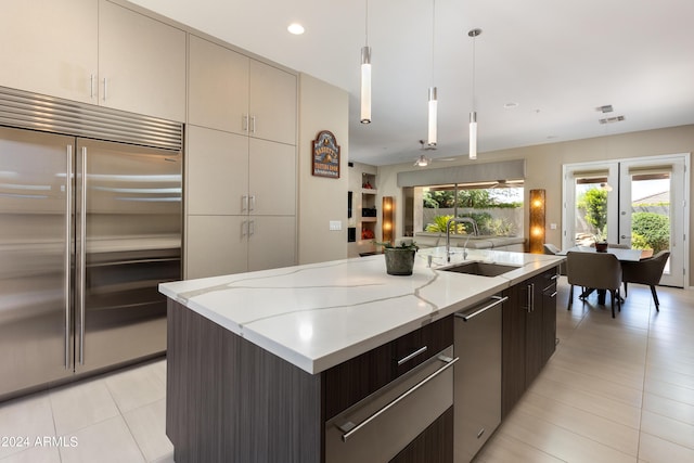 kitchen featuring a kitchen island with sink, a sink, hanging light fixtures, appliances with stainless steel finishes, and a warming drawer