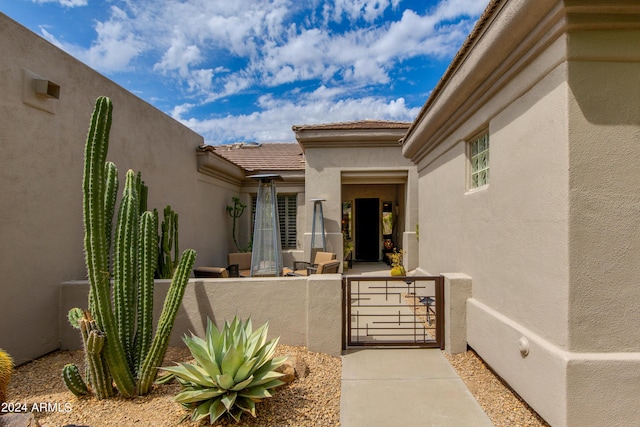 view of exterior entry featuring fence, a tile roof, a gate, and stucco siding