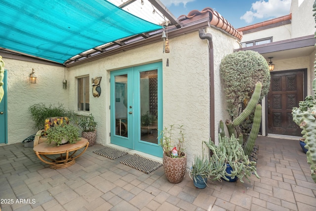 view of exterior entry with french doors, a patio area, a tile roof, and stucco siding