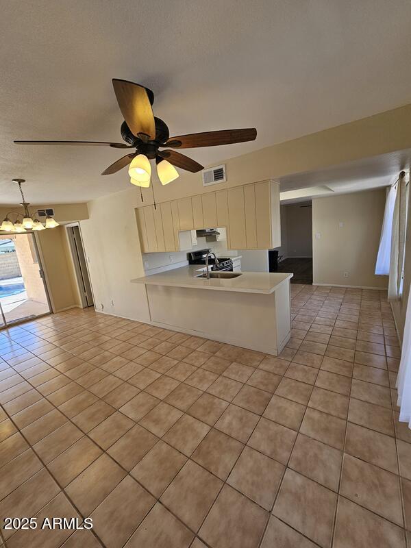 kitchen with light tile patterned floors, visible vents, a peninsula, light countertops, and a sink