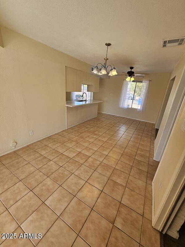 interior space featuring light tile patterned floors, visible vents, a textured ceiling, and ceiling fan with notable chandelier