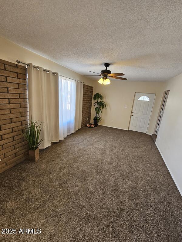 unfurnished living room with a textured ceiling, dark carpet, and a ceiling fan