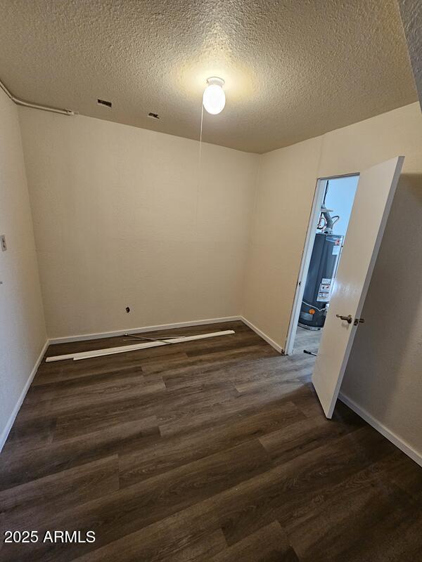 empty room with dark wood-style floors, water heater, a textured ceiling, and baseboards