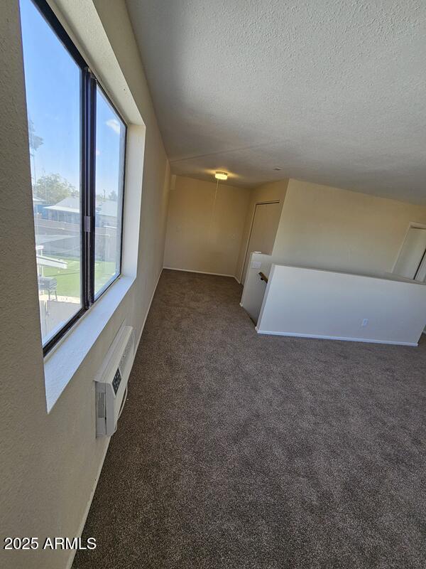 carpeted empty room featuring a wall unit AC and a textured ceiling