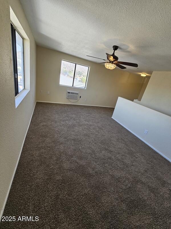 empty room featuring baseboards, a ceiling fan, a wall mounted air conditioner, carpet, and a textured ceiling