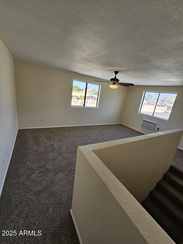 unfurnished room featuring stairway, carpet, a wall unit AC, and a healthy amount of sunlight