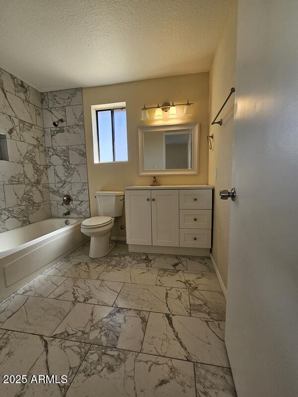 bathroom with marble finish floor, bathing tub / shower combination, toilet, a textured ceiling, and vanity