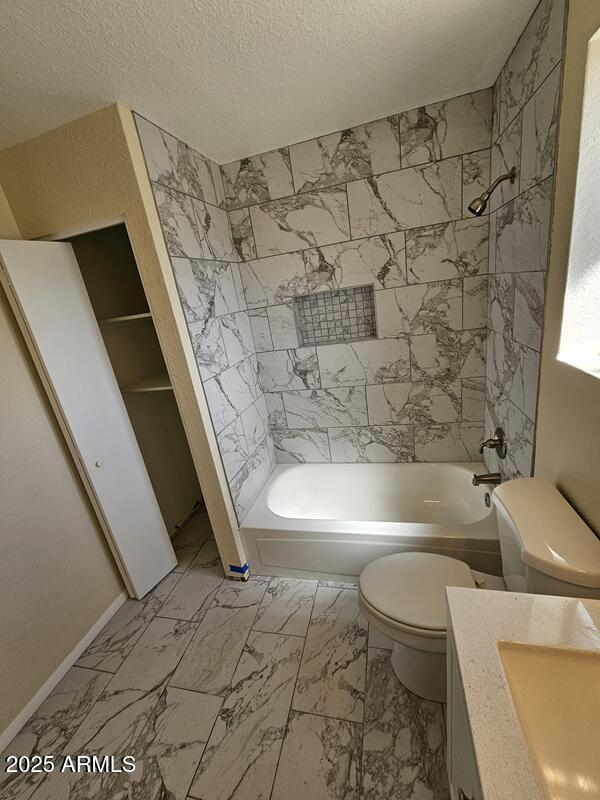 full bath featuring marble finish floor, toilet, washtub / shower combination, a textured ceiling, and vanity