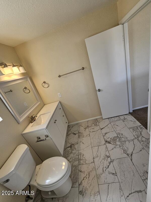 bathroom with a textured ceiling, toilet, vanity, baseboards, and marble finish floor