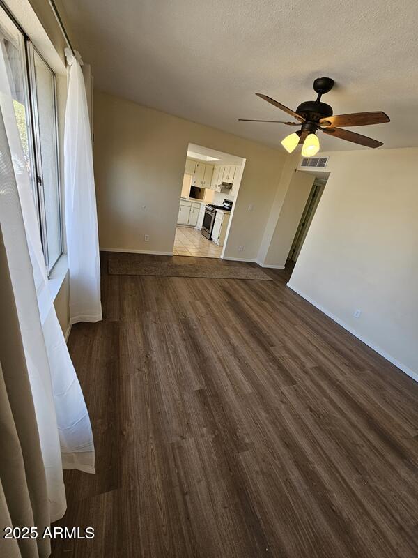 interior space featuring a textured ceiling, dark wood-type flooring, visible vents, baseboards, and a ceiling fan