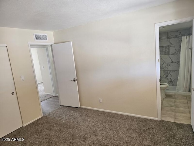 unfurnished bedroom featuring ensuite bath, carpet, visible vents, and baseboards