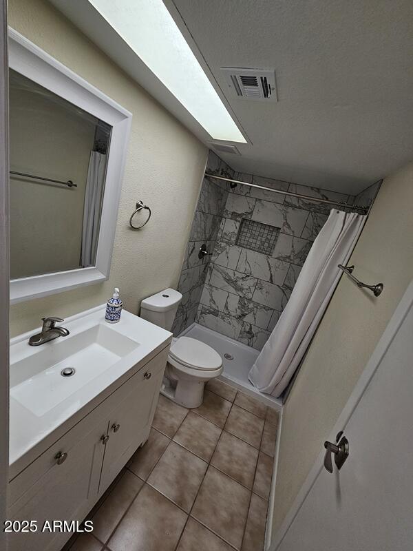 full bathroom with visible vents, toilet, a tile shower, vanity, and tile patterned flooring