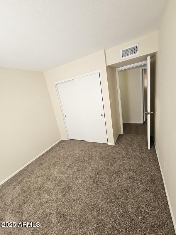 unfurnished bedroom featuring baseboards, carpet, visible vents, and a closet