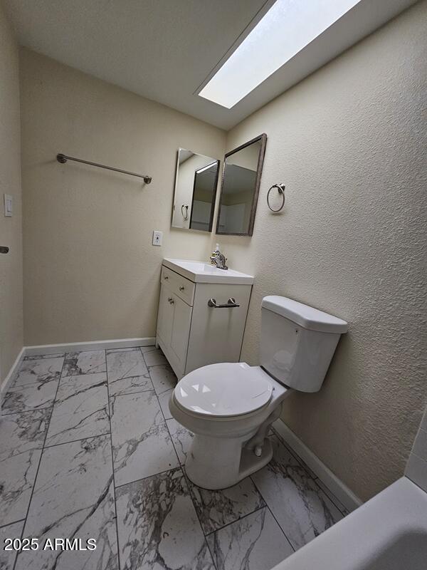 bathroom with marble finish floor, a skylight, and baseboards