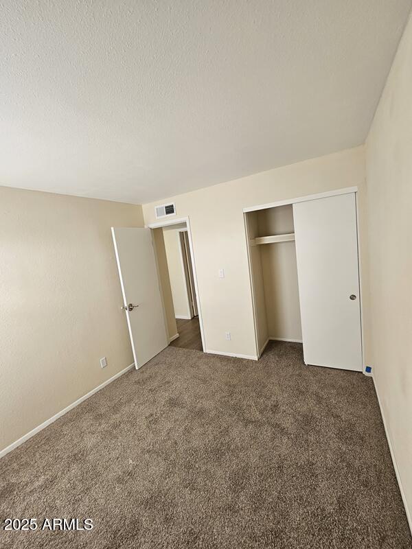 unfurnished bedroom featuring carpet, a closet, visible vents, and a textured ceiling