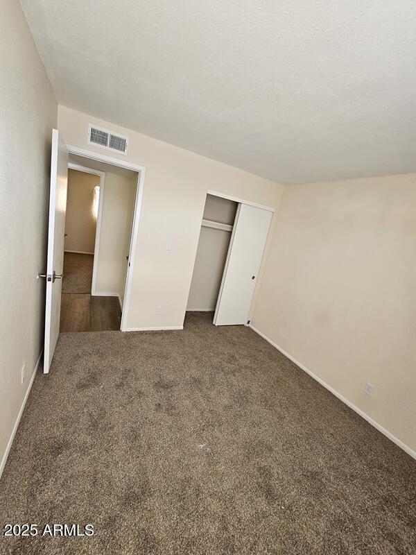 unfurnished bedroom featuring a closet, visible vents, carpet flooring, a textured ceiling, and baseboards