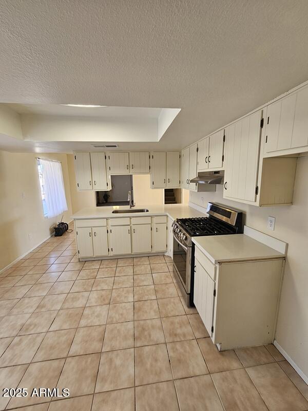 kitchen featuring light tile patterned floors, a sink, gas range, and under cabinet range hood