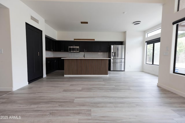 kitchen with visible vents, appliances with stainless steel finishes, a kitchen island with sink, light countertops, and dark cabinetry