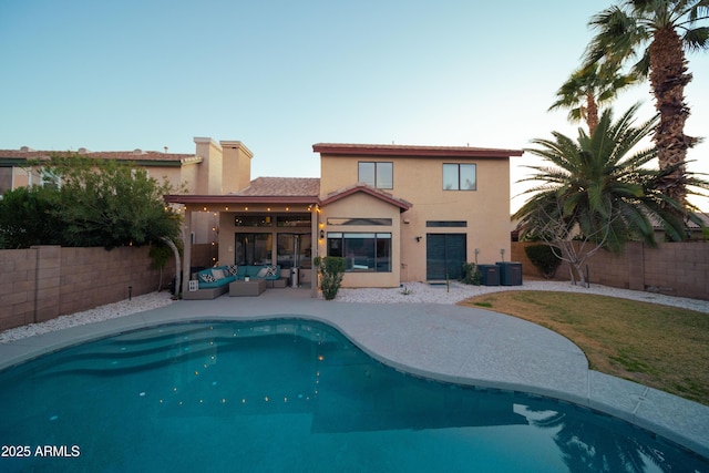 rear view of house with a fenced in pool, a fenced backyard, an outdoor living space, and stucco siding