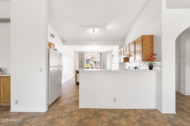 kitchen featuring freestanding refrigerator, arched walkways, a peninsula, under cabinet range hood, and light countertops