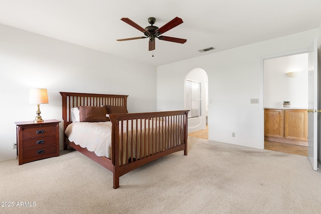bedroom with light carpet, arched walkways, ensuite bathroom, and a ceiling fan