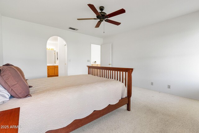 bedroom featuring arched walkways, light carpet, ceiling fan, and ensuite bathroom