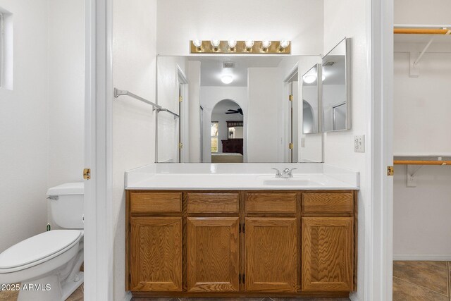 full bathroom featuring toilet, a walk in closet, vanity, and tile patterned flooring