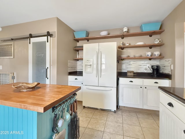 kitchen featuring white fridge with ice dispenser, a barn door, a center island, wood counters, and white cabinetry