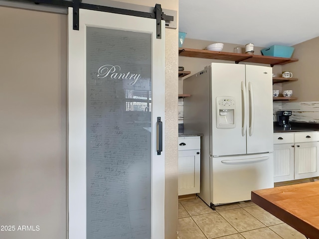 kitchen featuring white cabinets, light tile patterned floors, a barn door, and white fridge with ice dispenser