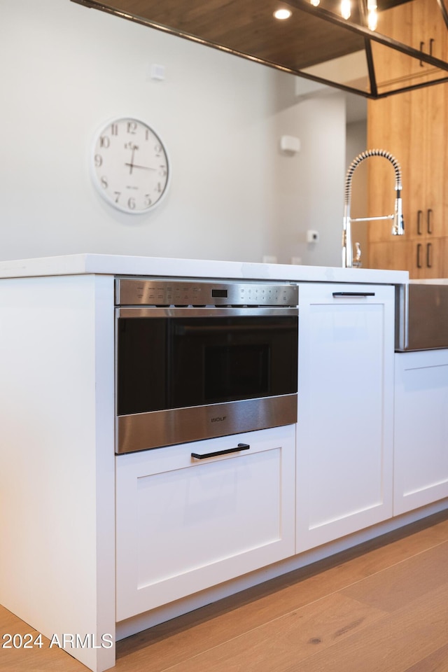 kitchen featuring light wood-type flooring, white cabinetry, and stainless steel oven