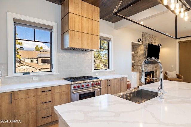 kitchen featuring a healthy amount of sunlight, a stone fireplace, decorative backsplash, and luxury stove