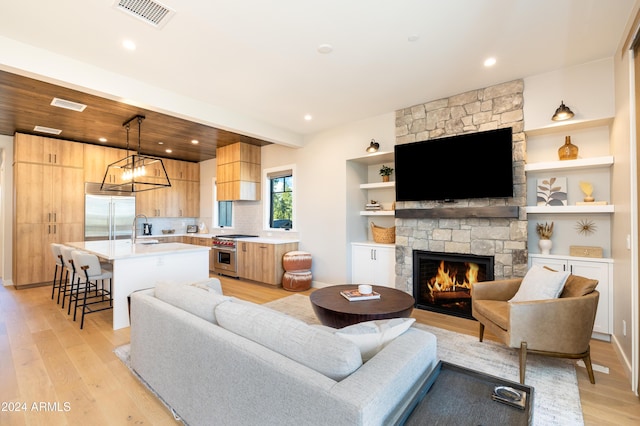 living room featuring a stone fireplace, light hardwood / wood-style flooring, built in features, and sink