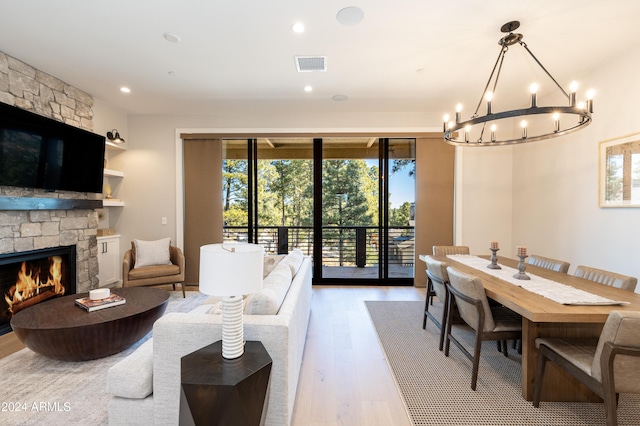 living room with a notable chandelier, a healthy amount of sunlight, a stone fireplace, and light hardwood / wood-style flooring