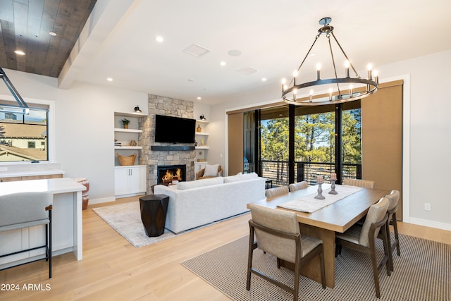 dining room featuring a fireplace, built in shelves, light hardwood / wood-style flooring, and a notable chandelier