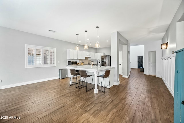 kitchen featuring a breakfast bar area, decorative light fixtures, stainless steel appliances, hardwood / wood-style floors, and white cabinets