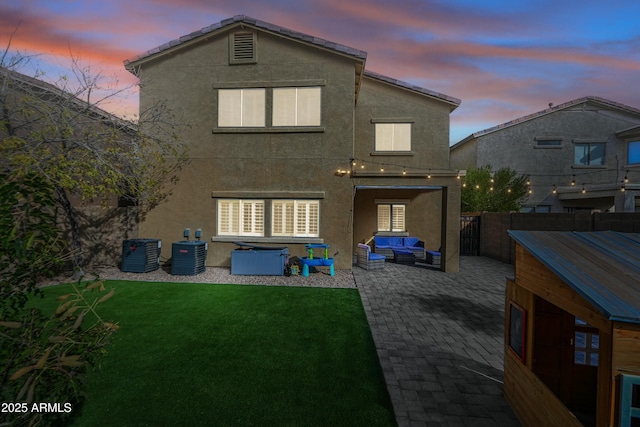 back house at dusk with an outdoor living space, a patio, central AC, and a lawn